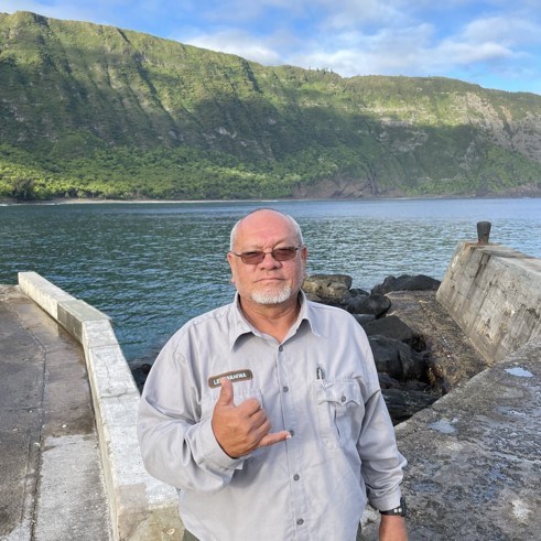 Joseph Leihiwahiwa Kaiama Jr. Man in front of a green mountain and water