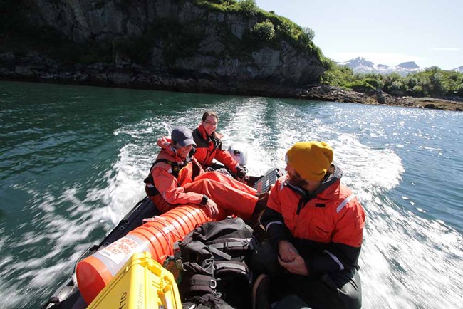 Three people in a small boat loaded with field gear.