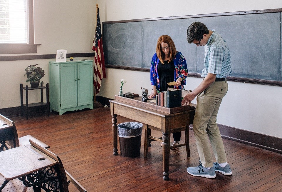 Two visitors at a teacher's desk in a classroom