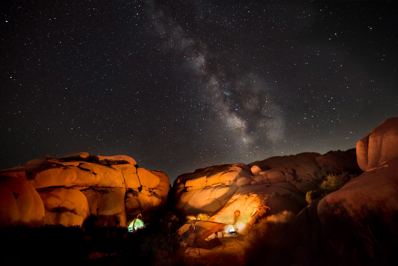 Tents by rock outcropping at night under the Milky Way
