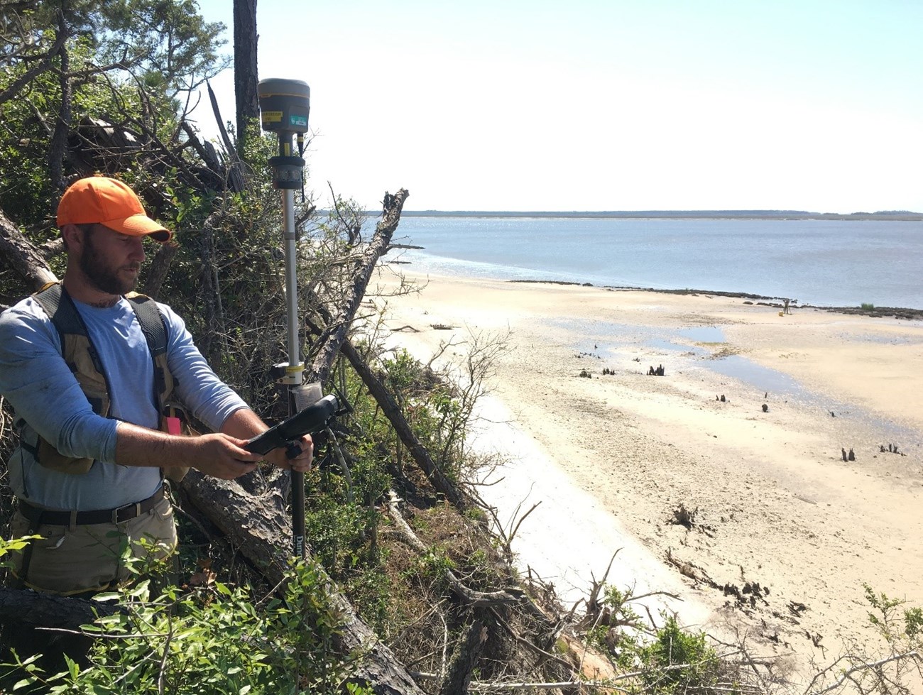 Man holds a small device near the shoreline