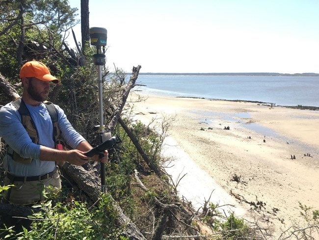 Man holds a small device near the shoreline