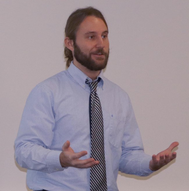 Jake McDonald's dissertation defense. Jake wearing a shirt and tie standing with arms open.