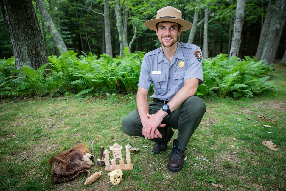 Uniformed park ranger kneels by a pile of interpretive props