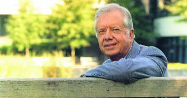 Ex-president, Jimmy Carter, poses next to a ranch fence on a sunny day.