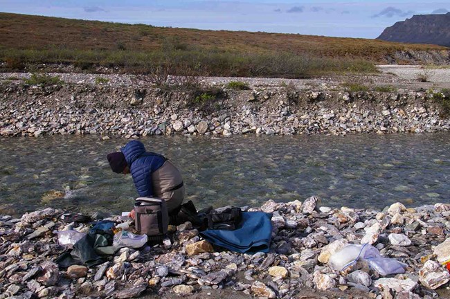 A researcher collects water data along an arctic stream.