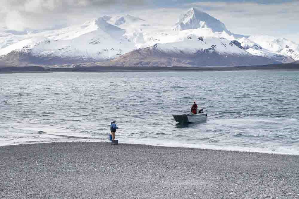 A researcher in a bout comes to meet another researcher on shore.