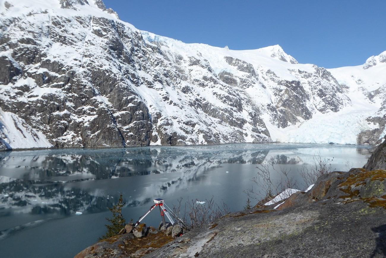 A camera on a tripod pointed at a tidewater glacier