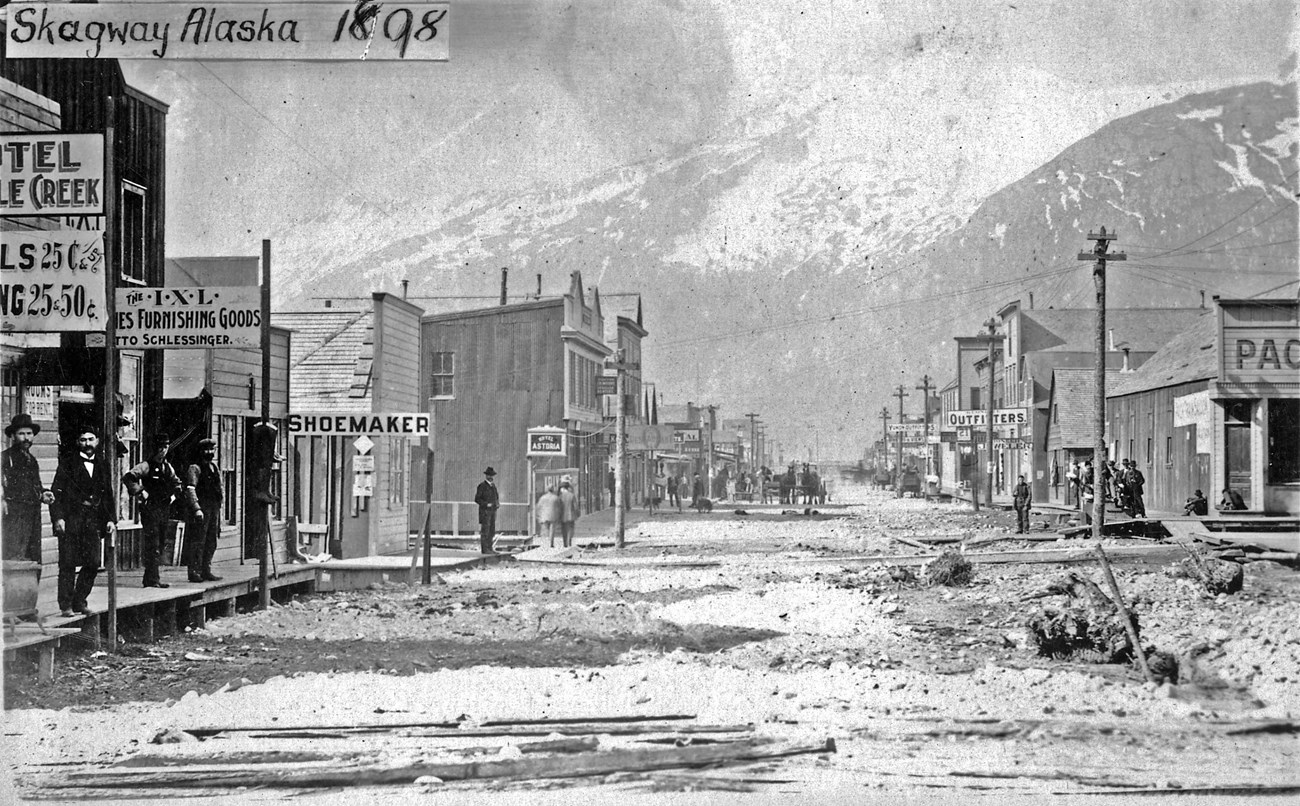 A street scene. Stores lining the left and right of the street with mountains in the background.