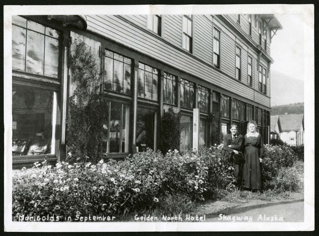 lt= Two residents stand next to their marigolds outside the Gold North Hotel.