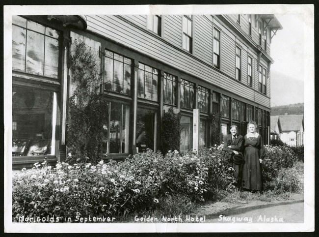 Two residents stand next to their marigolds outside the Gold North Hotel.