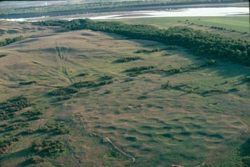 Aerial view shows a pattern of shallow depressions in an open green and brown landscape near a river