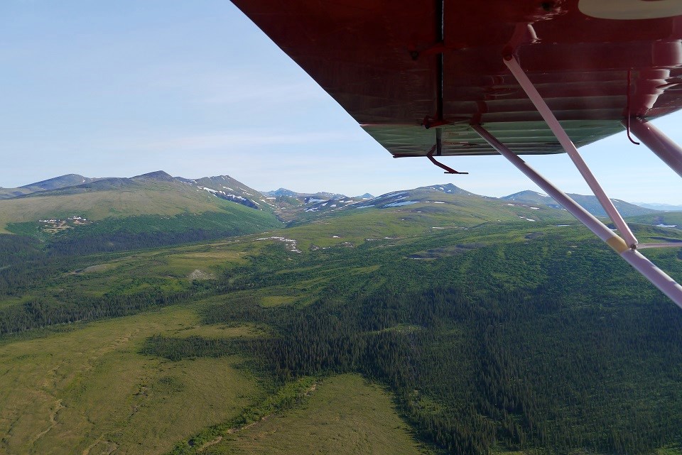Wing tip of a plane flying over green mountains