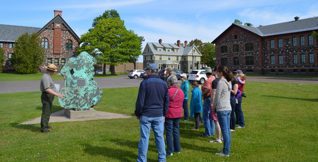 A ranger points at a large chunk of copper while a group of people looks on.