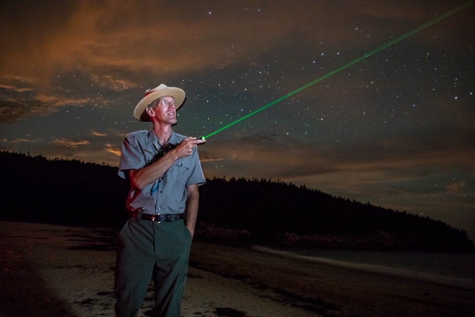 Uniformed park ranger uses a laser pointer across night skies Uniformed park ranger uses a laser pointer across night skies