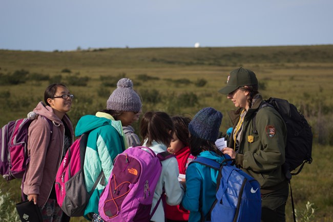 A group of students stand in a large grassy field with a ranger.