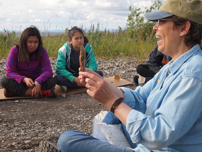 youth and an older woman sitting in a circle on gravel