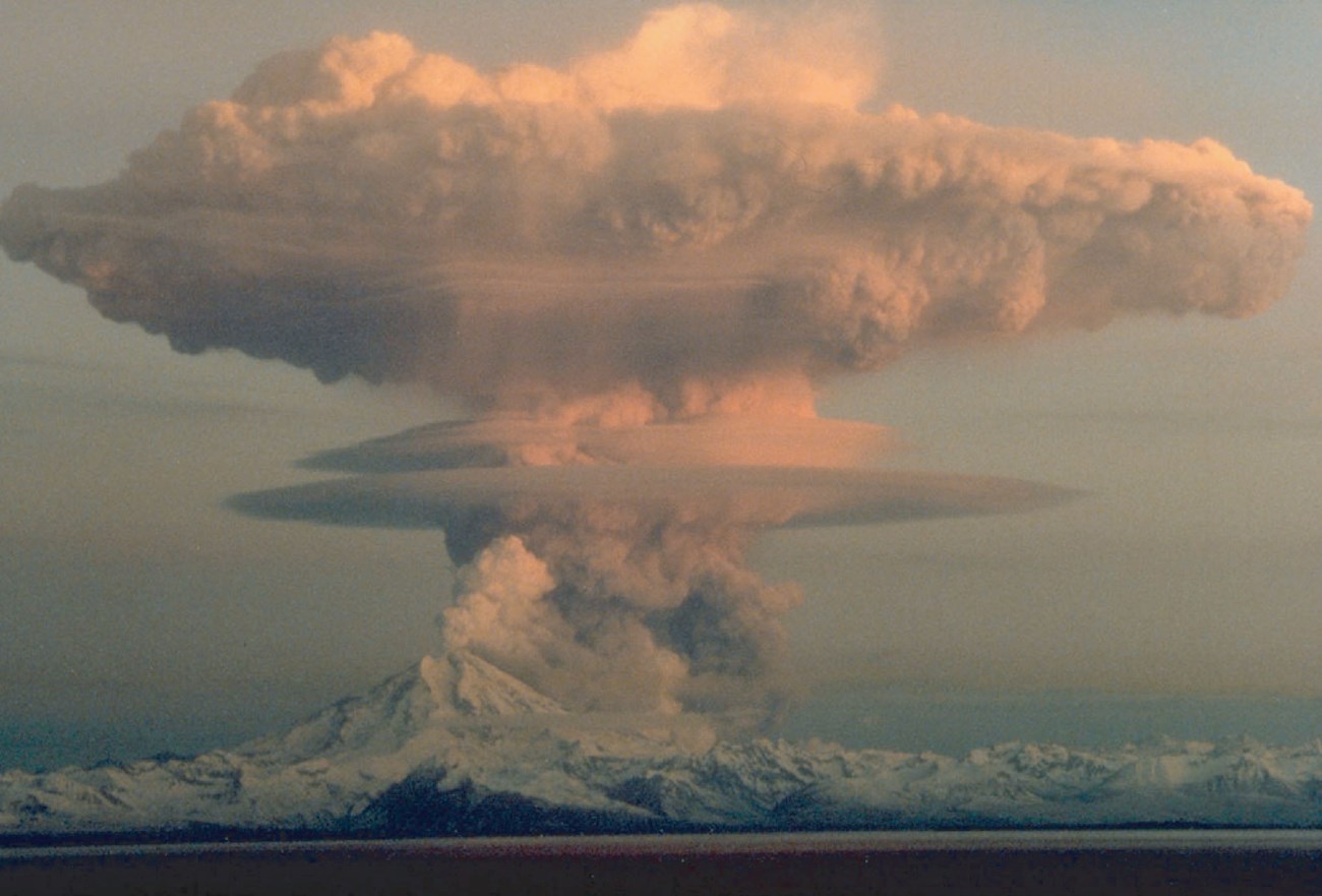 snow covered volcano peak erupting large cloud of ash and steam