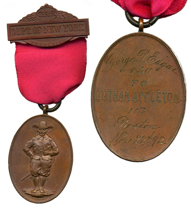 Front and back views of oval bronze-colored medal with figure of man and engraving, hanging on red ribbon