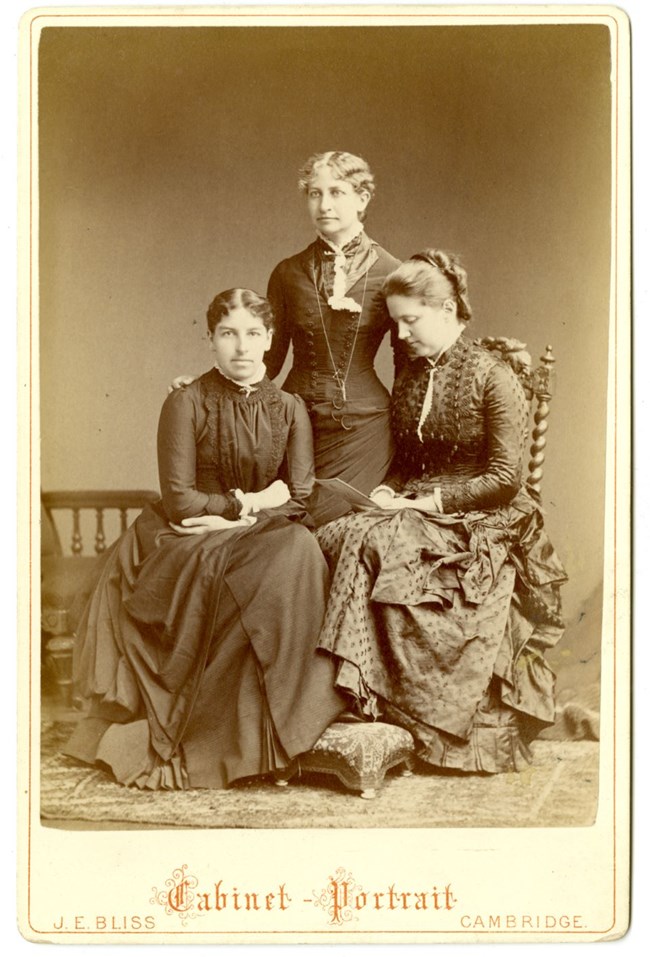 Three women in black and white studio portrait, two seated and one standing
