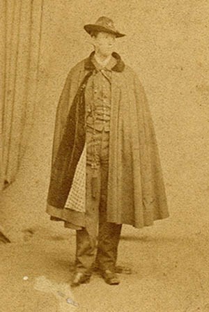 Studio photograph of young man standing in military uniform with long cape