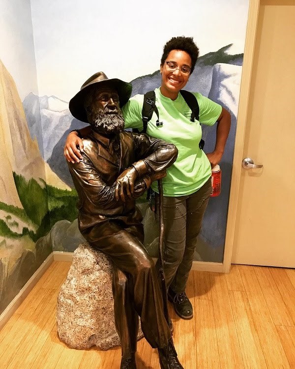 A young woman stands next to a John Muir statue.