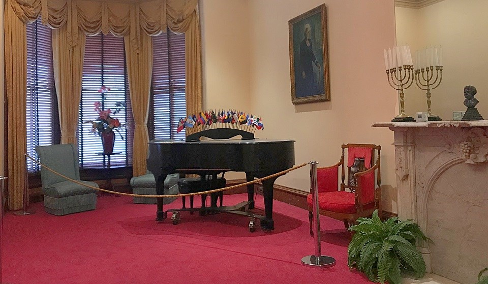 MAMC Parlor Edit Parlor with a piano, red carpet, fireplace, chandelier, and painting of Mary McLeod Bethune