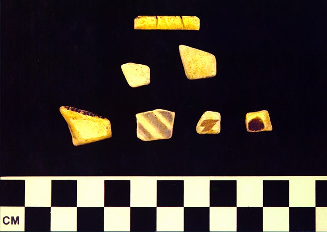 At bottom are four edge-worn, geometrically shaped ceramics. Two pebbles in the middle and one rectangular bone piece at the top.
