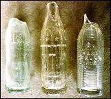 Three clear glass soda bottles from different brands