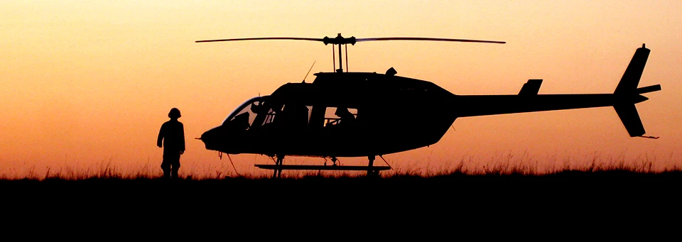 Helicopter at sunset - Mesa Verde National Park A helicopter sits on the ground as a person in a flight suit walks in front of it during sunset.