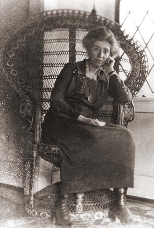 Full length photo of Mary Colter sitting in an elaborate wicker chair that wraps around her.