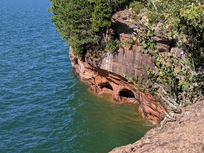 View of steep cliffs with carved caves at the water line.