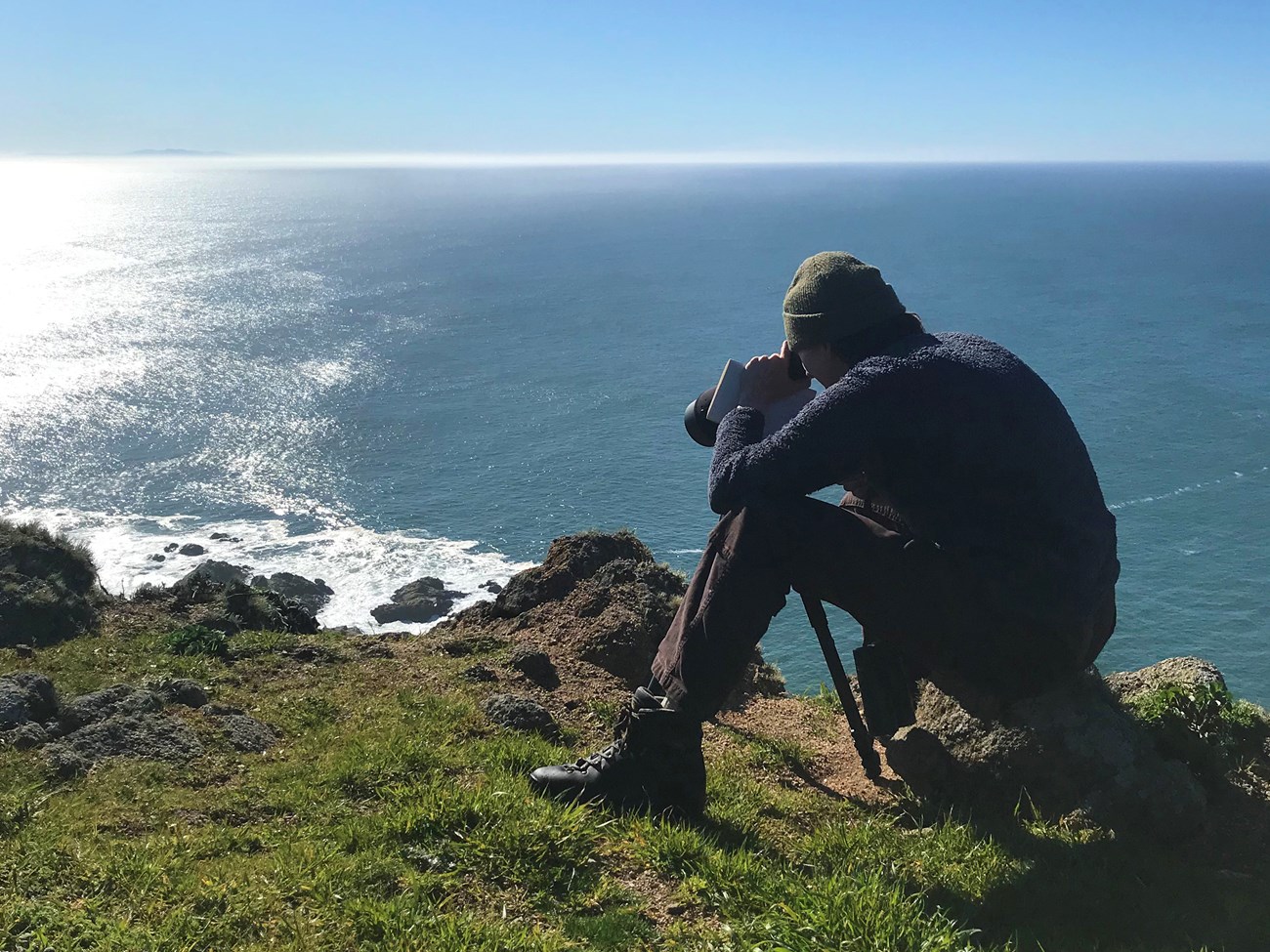 Researcher counting seals A person sits at a cliff edge while looking through a telescope.