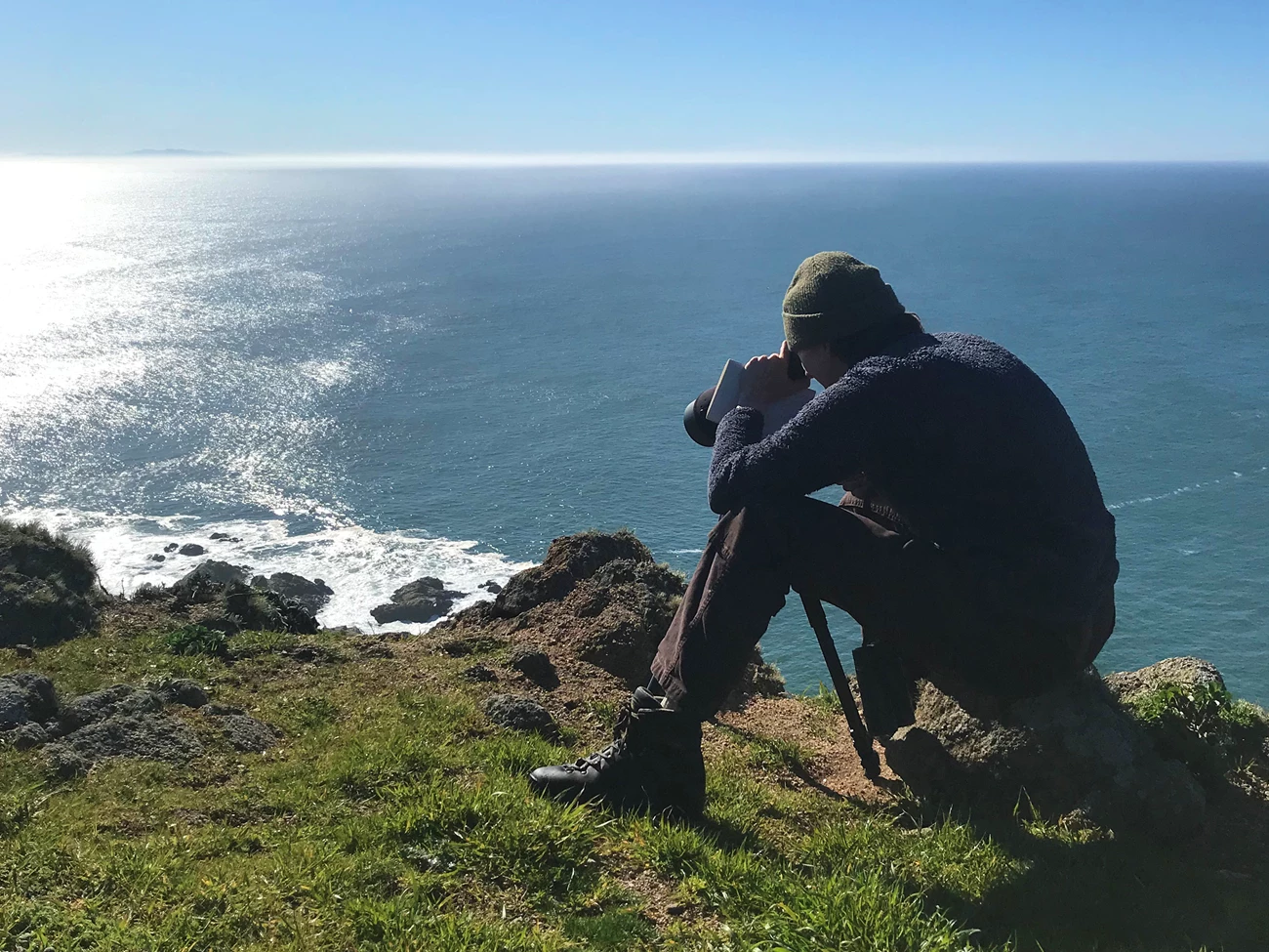 Researcher counting seals A person sits at a cliff edge while looking through a telescope.