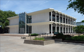 Large, white stone building with black windows and a pond in front.