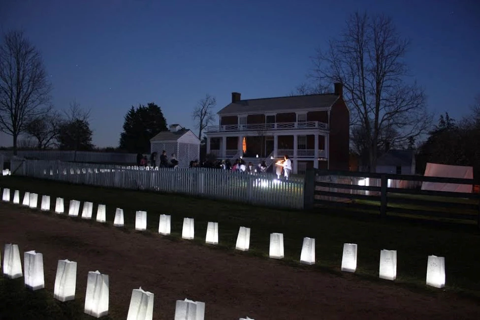 McLean House Luminaries A small two story historic home with a small white fence. Paper Luminaries line the front yard at night.