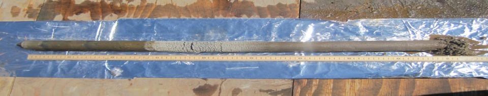 A long narrow core of sediment lies next to a long ruler on a sheet of tin foil.