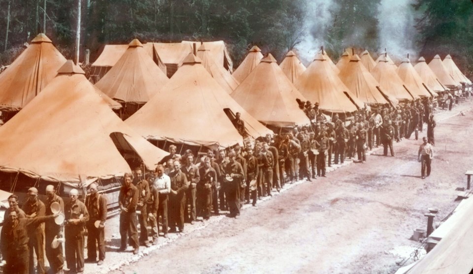 Colorized black and white photo of tents and men in uniforms standing in a line.