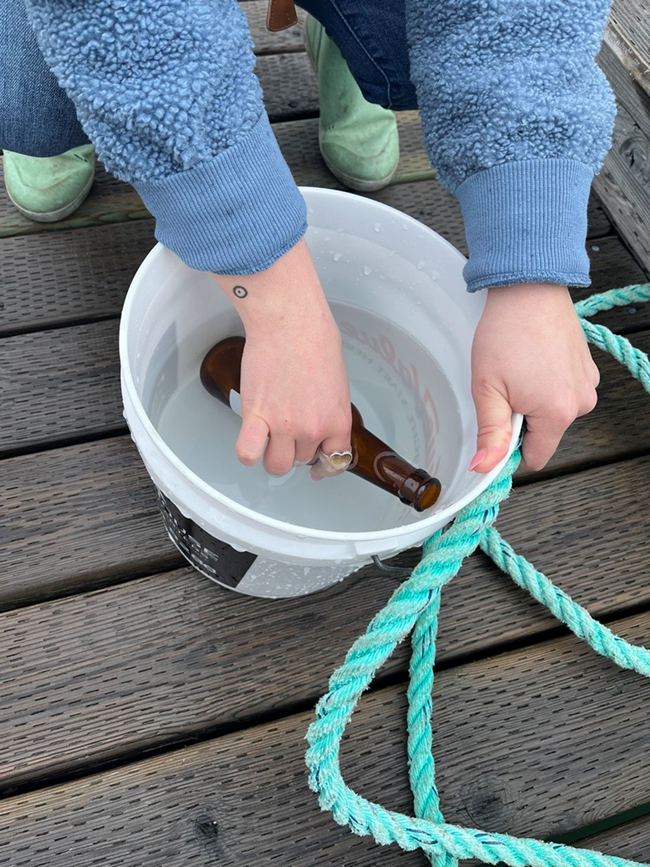 A person takes a sample of water from a bucket into a brown glass bottle