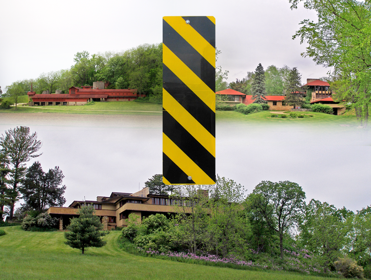 Red buildings on a hill and a brown building on a hill with a yellow and black rectangle sign in the middle.