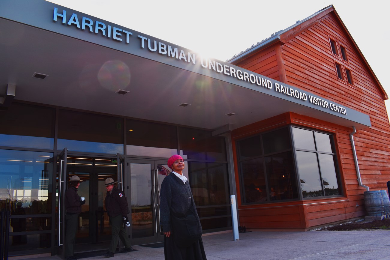 An older African American woman dressed as Harriet Tubman, stands in front of the visitor center.