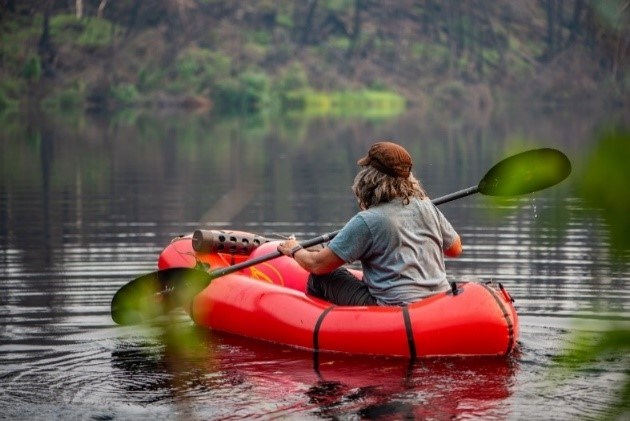 A woman paddles in a lake in a red inflatable raft.