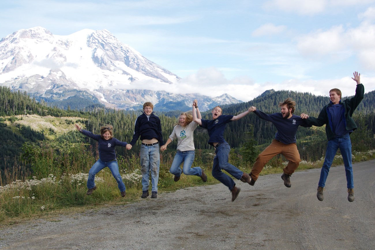 Kids jump and smile, a tall mountain, mount rainier, is behind them