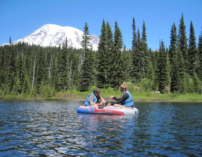 Two people in a small inflated boat floating in a mountain lake.