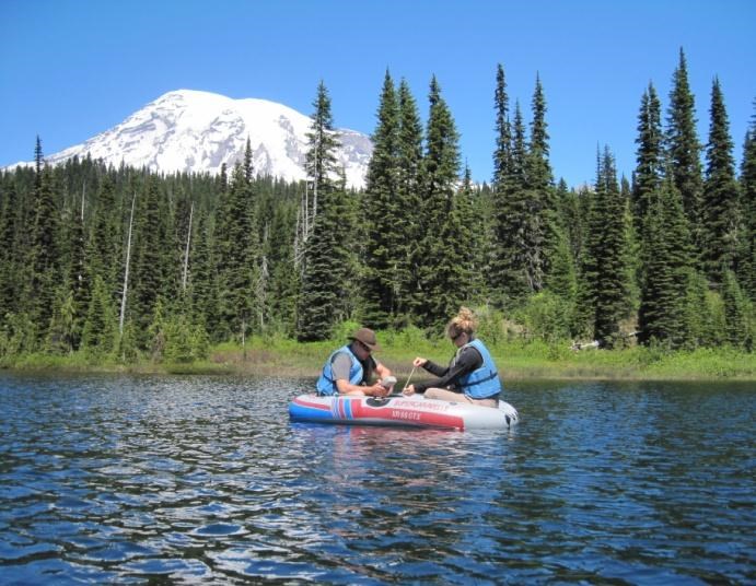 Field sampling Two people in a small inflated boat floating in a mountain lake.