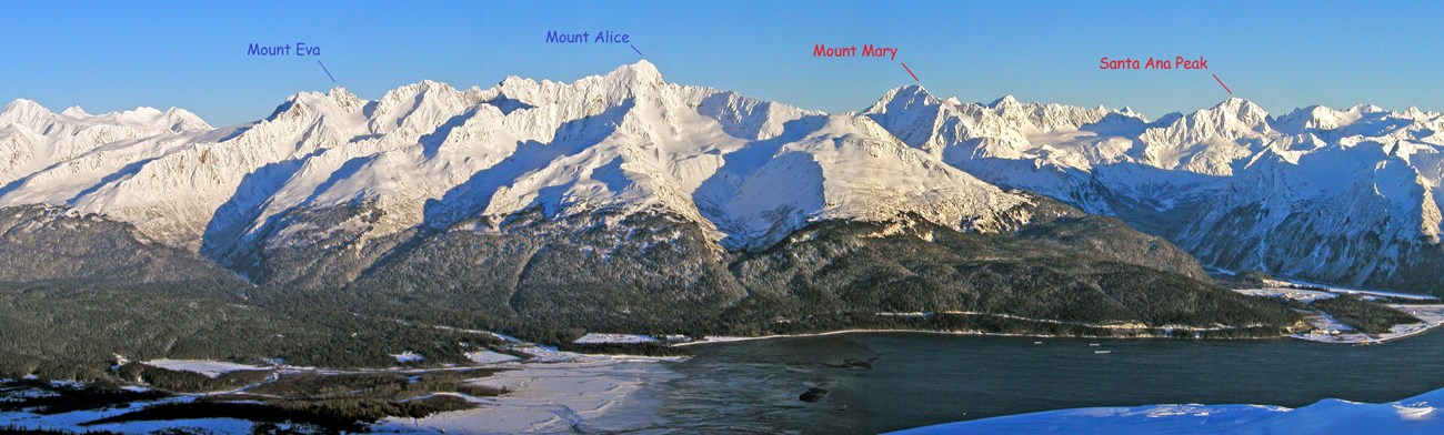 Four snow-covered peaks rise above a shallow bay.