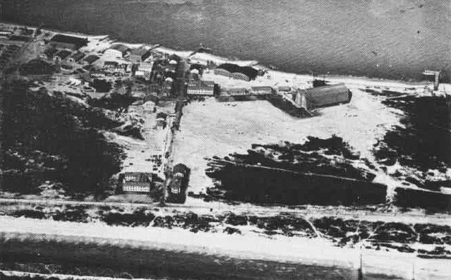 Grainy black-and-white photo of buildings clustered around beachfront