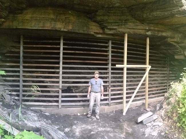 A man standing next to a mine portal with a large gate covering the entrance. A man standing next to a mine portal with a large gate covering the entrance.