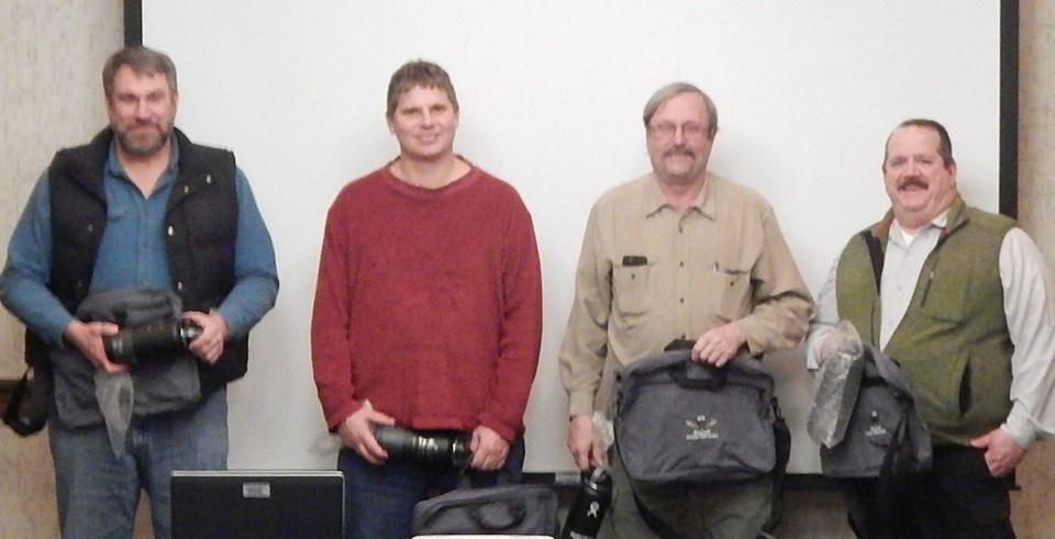 Four men stand in front of screen.