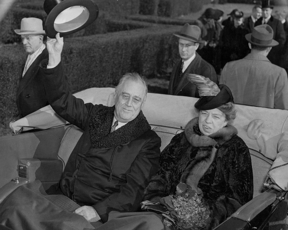 A man and women in open car greeted by crowds lining a street.